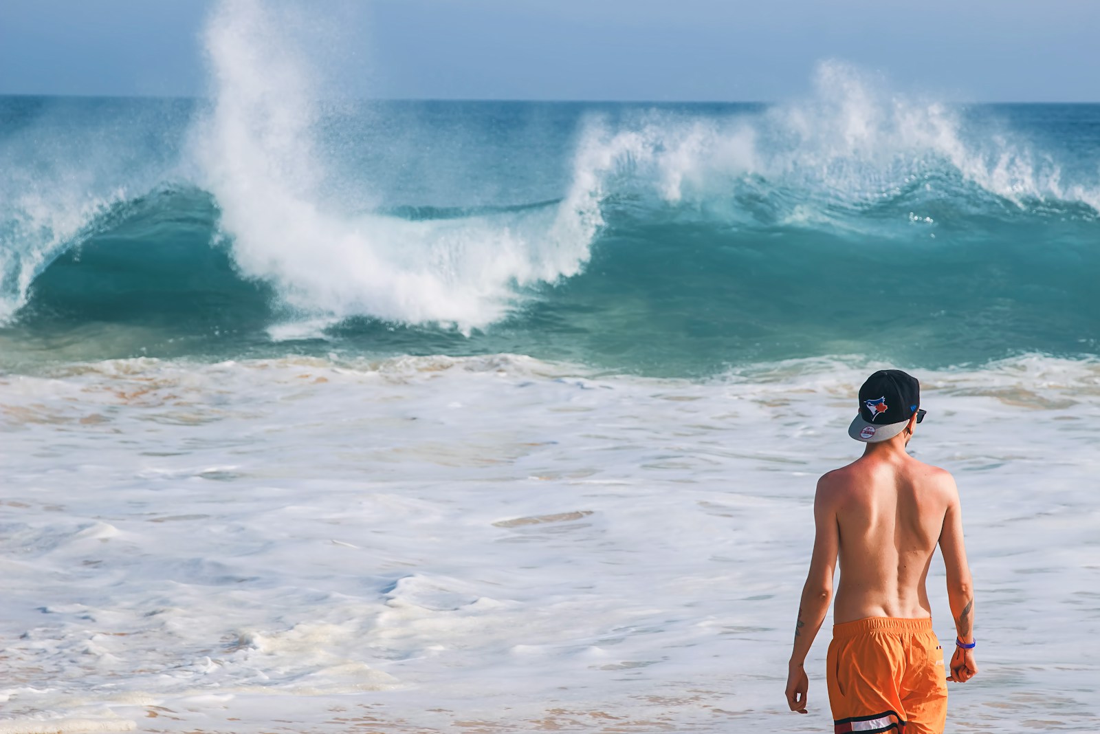 man in orange shorts standing near wavy sea during daytime